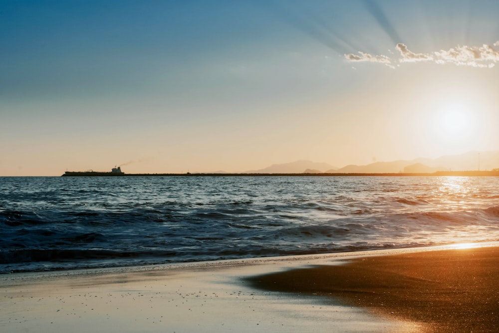 the sun is setting over the ocean with a ship in the distance