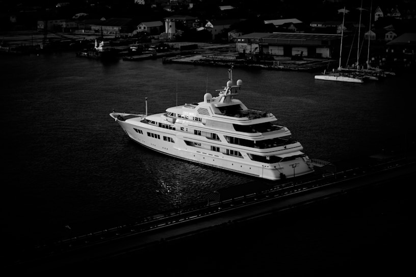 Black and white photo of a sleek luxury yacht gently anchored on calm waters at dusk.