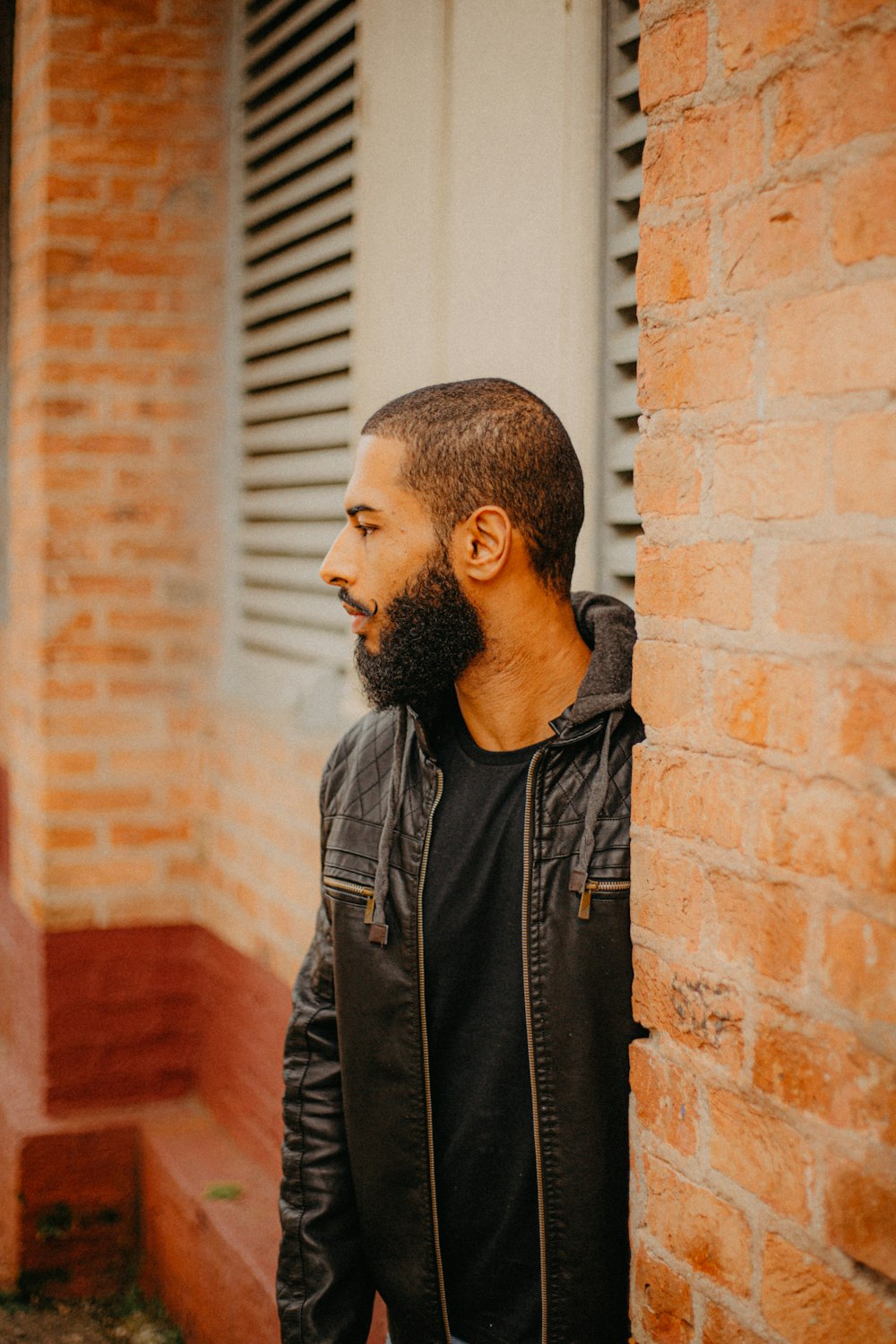 a man with a beard standing next to a brick wall