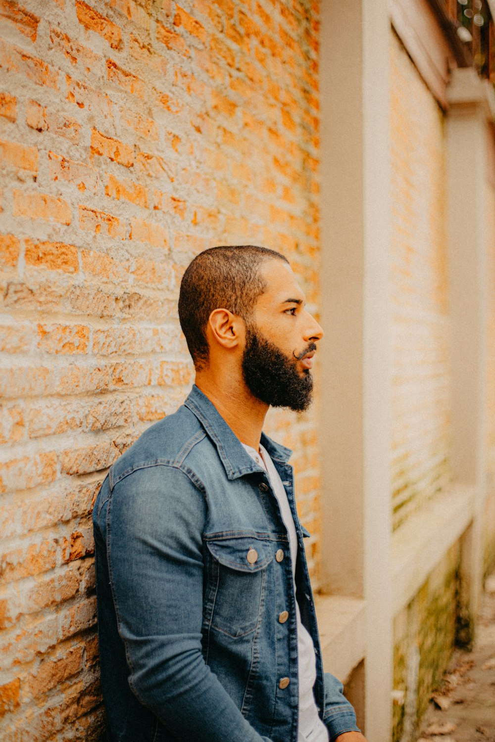 a bearded man leaning against a brick wall