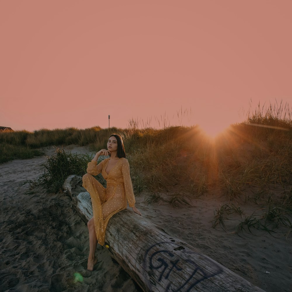 a woman sitting on a log in the sand