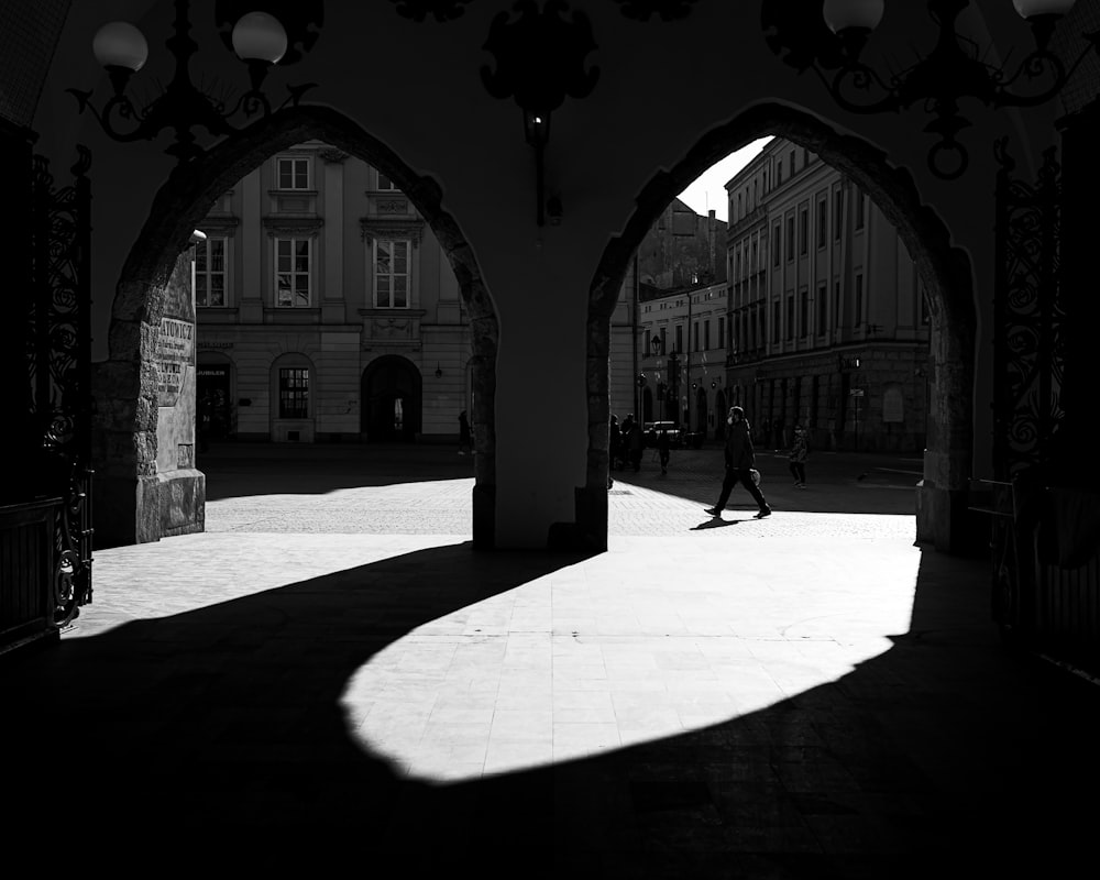 a black and white photo of a person walking through an archway