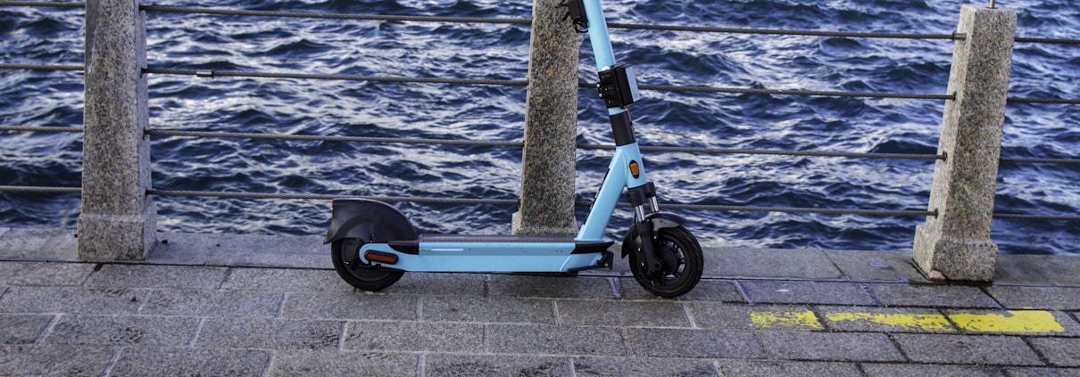 a blue scooter parked on a sidewalk next to a body of water