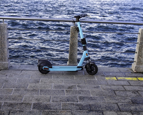 a blue scooter parked on a sidewalk next to a body of water