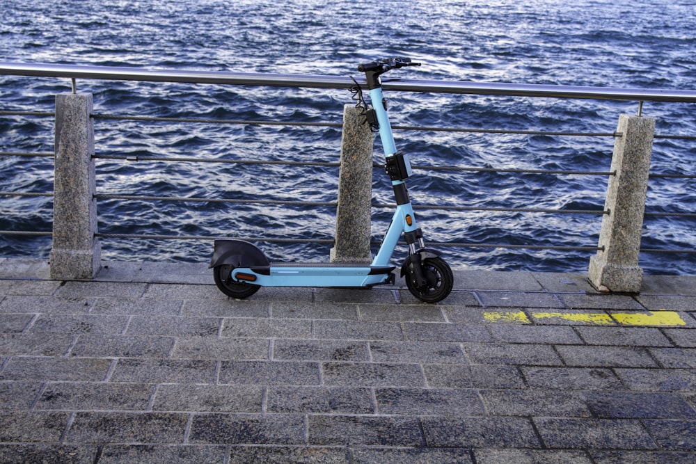 a blue scooter parked on a sidewalk next to a body of water