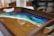A wooden tray with a resin art design featuring a vibrant seascape pattern in shades of blue, green, and white. The colors appear to blend seamlessly, resembling an ocean scene with a sandy shore.