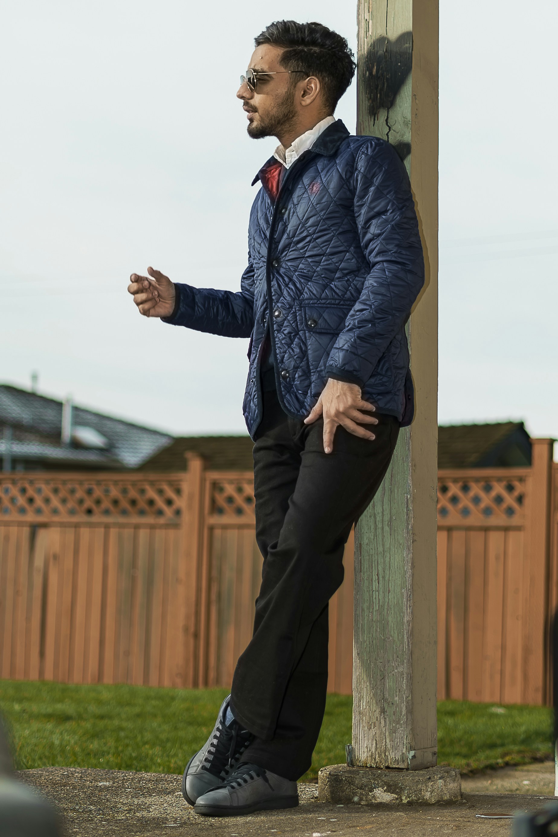 a man in a blue jacket leaning against a pole