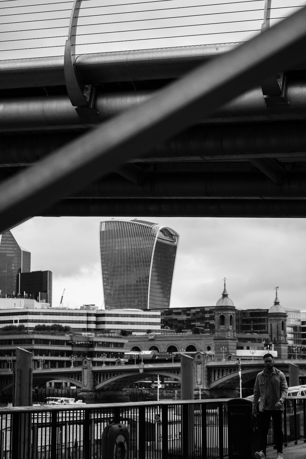 a black and white photo of a man standing under a bridge