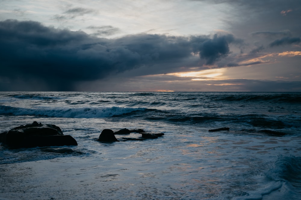 the sun is setting over the ocean with dark clouds