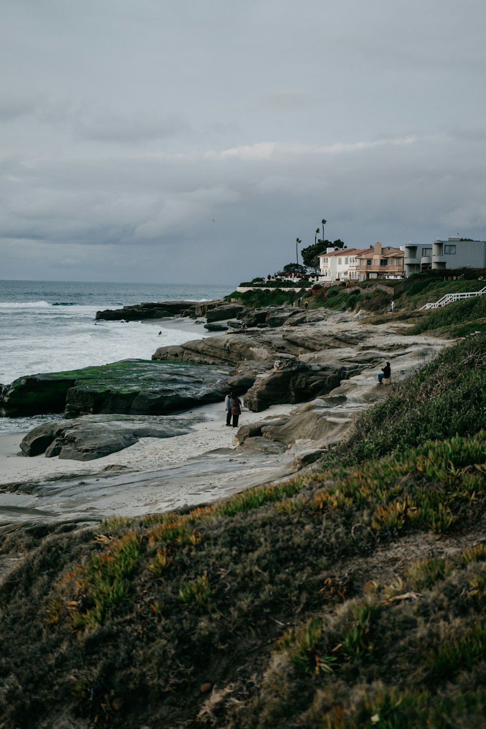 um par de pessoas em pé no topo de uma praia ao lado do oceano