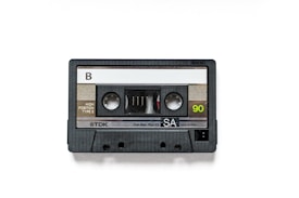 A black audio cassette tape with a side labeled 'B' and marked with 'TDK', 'SA', and '90' written on it. The housing is made of plastic with a clear window exposing the tape reels inside.