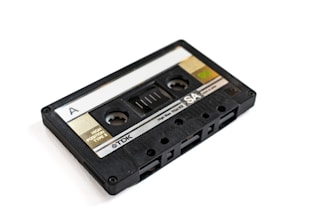 A vintage cassette tape with a black plastic casing and a transparent window, labeled with 'A' on one side and branding information including 'TDK' and 'SA'. The tape has visible spools and labeling indicating 'High Position Type II' and other technical specifications.