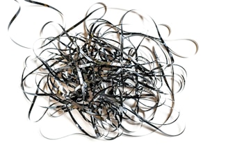 A chaotic tangle of black and shiny film tape sprawled across a white background, forming intricate loops and twists.