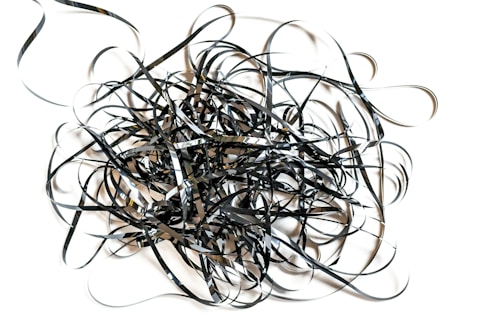 A chaotic tangle of black and shiny film tape sprawled across a white background, forming intricate loops and twists.
