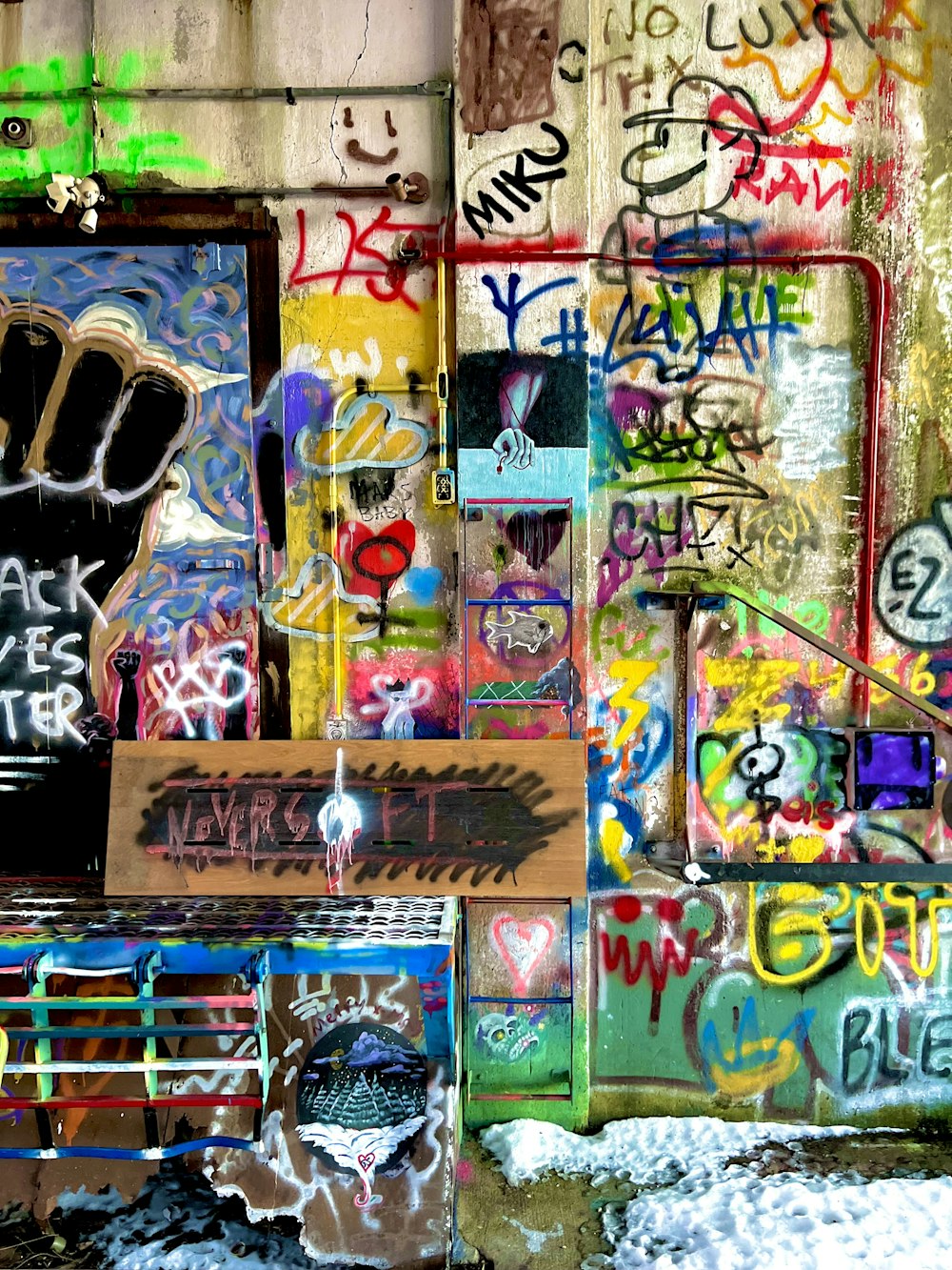 a wall covered in lots of graffiti next to a building