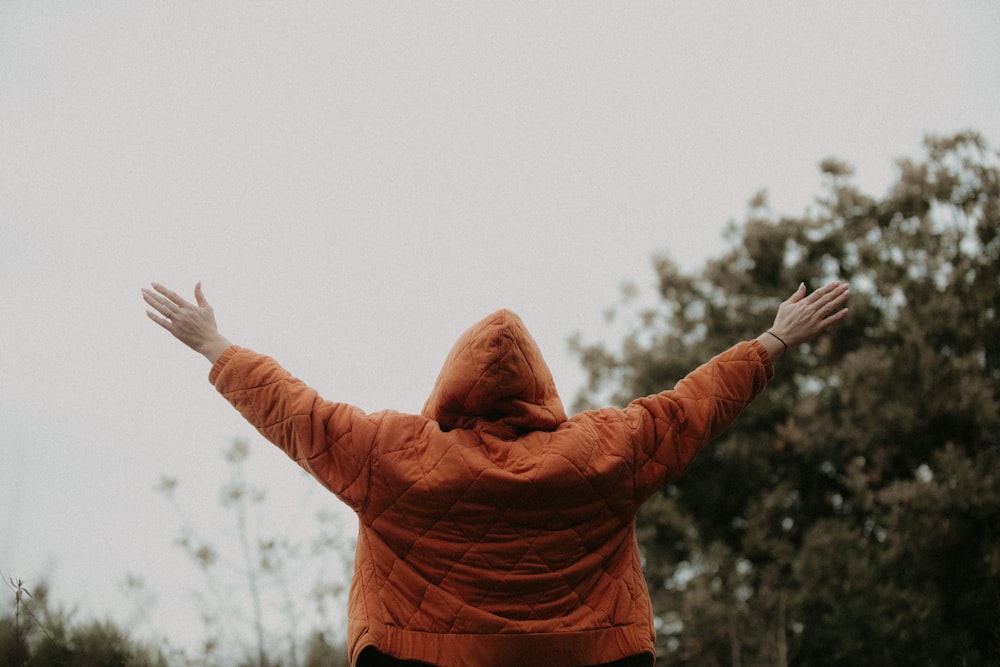 a person in an orange jacket is flying a kite