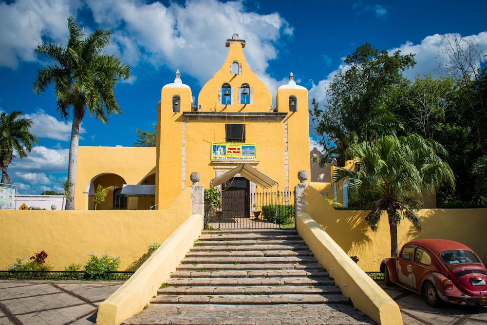 a red car parked in front of a yellow church