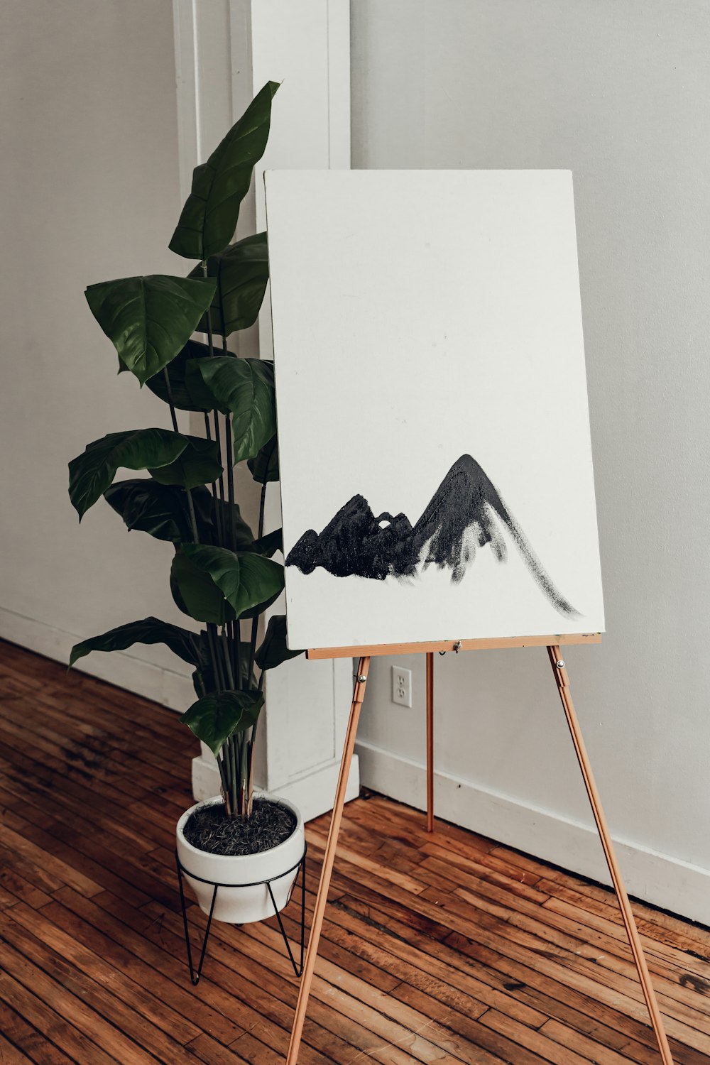 a painting on a easel next to a potted plant