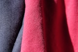 Three pieces of fabric are draped together, featuring a textured, woven pattern. The fabrics display a smooth, tightly knit appearance in shades of dark blue, pink, and red, all illuminated by light that accentuates their intricate textures.