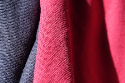 Three pieces of fabric are draped together, featuring a textured, woven pattern. The fabrics display a smooth, tightly knit appearance in shades of dark blue, pink, and red, all illuminated by light that accentuates their intricate textures.