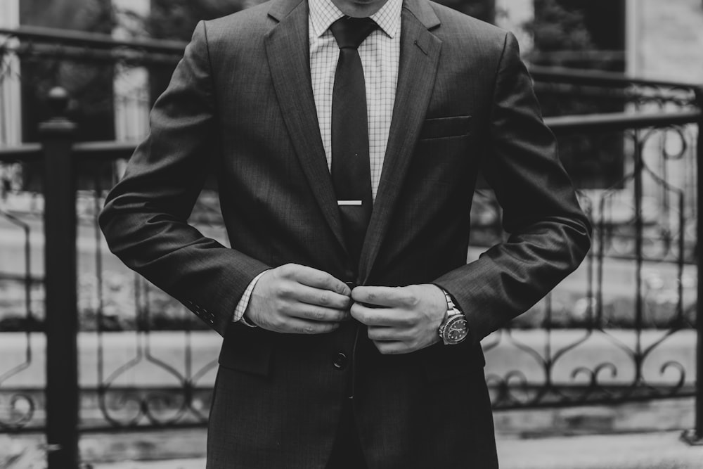 a man in a suit and tie standing in front of a fence