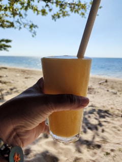 Close-up of a hand holding a fresh green smoothie with the ocean in the background.