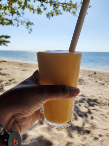 Close-up of a hand holding a fresh green smoothie with the ocean in the background.