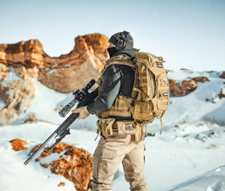 a man with a rifle standing on top of a snow covered mountain