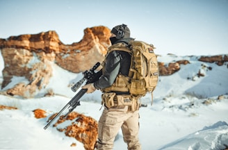 a man with a rifle standing on top of a snow covered mountain