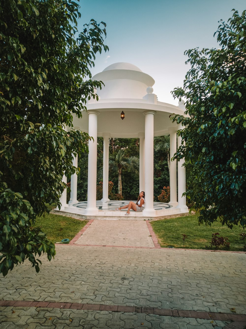 a woman sitting in a white gazebo surrounded by trees