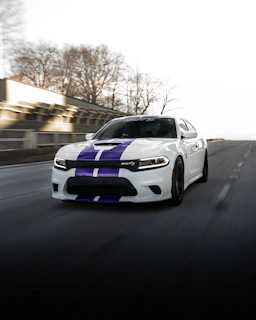 White car with purple stripes driving on road