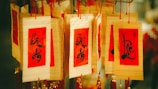 Several decorative cards with red and golden backgrounds, featuring intricate black calligraphy, are hanging. They are strung together with red threads and adorned with additional red and gold tassels.