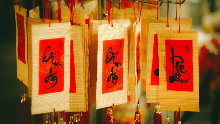 Several decorative cards with red and golden backgrounds, featuring intricate black calligraphy, are hanging. They are strung together with red threads and adorned with additional red and gold tassels.