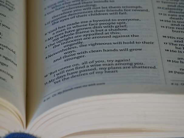 An open book with text in a serif font is visible, showing paragraphs separated by numbers. The focus is on a section written in verse format. The pages appear slightly curved, giving a three-dimensional effect.