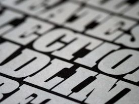 A close-up view of bold, black and white text with a slightly blurred effect, giving the impression of a print or poster design. The letters are large and occupy much of the frame, creating a striking visual impact.