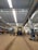A large industrial train workshop with high ceilings, showcasing a train car undergoing maintenance. The space is organized with various tools and equipment scattered around, along with workers in the background attending to their tasks. The lighting is bright, with overhead lights reflecting off the metallic surfaces.