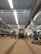A large industrial train workshop with high ceilings, showcasing a train car undergoing maintenance. The space is organized with various tools and equipment scattered around, along with workers in the background attending to their tasks. The lighting is bright, with overhead lights reflecting off the metallic surfaces.