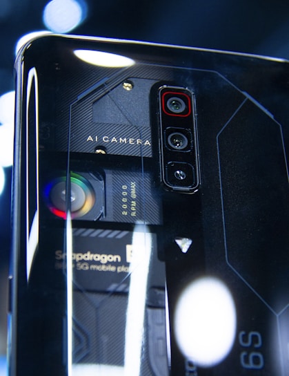 A close-up view of a smartphone's back panel showcasing its triple camera setup and other technical components. The text 'AI Camera' and 'Snapdragon' can be seen on the phone, along with visible lenses and intricate design patterns in a futuristic style.