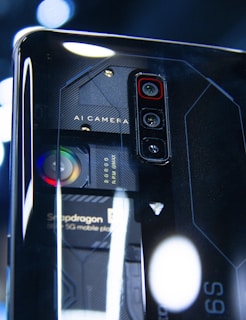 A close-up view of a smartphone's back panel showcasing its triple camera setup and other technical components. The text 'AI Camera' and 'Snapdragon' can be seen on the phone, along with visible lenses and intricate design patterns in a futuristic style.