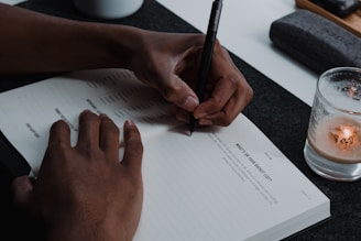 a person writing on a notepad next to a glass of water