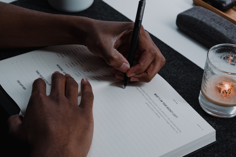 a person writing on a notepad next to a glass of water