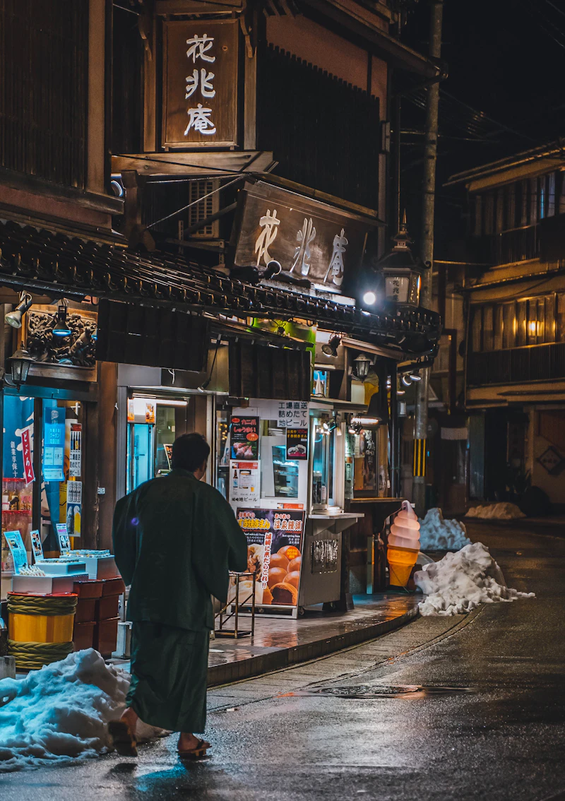 A Japanese man walking through the lantern-lit streets of Kinosaki Onsen at night, wearing a yukata