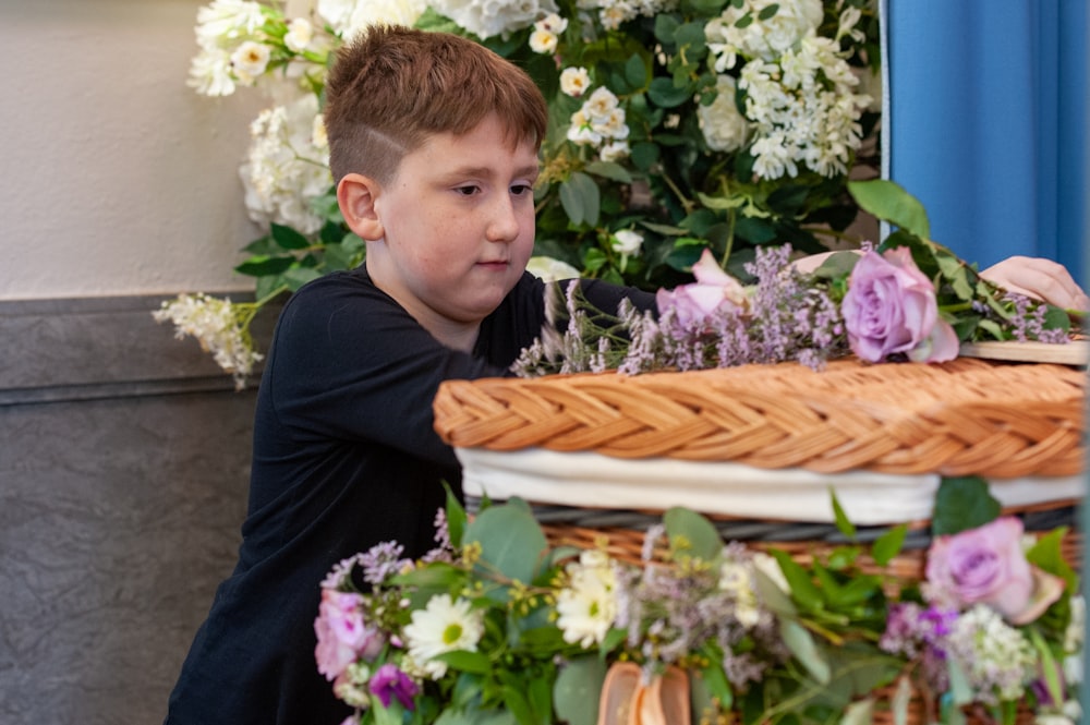 a young boy sitting in front of a basket of flowers