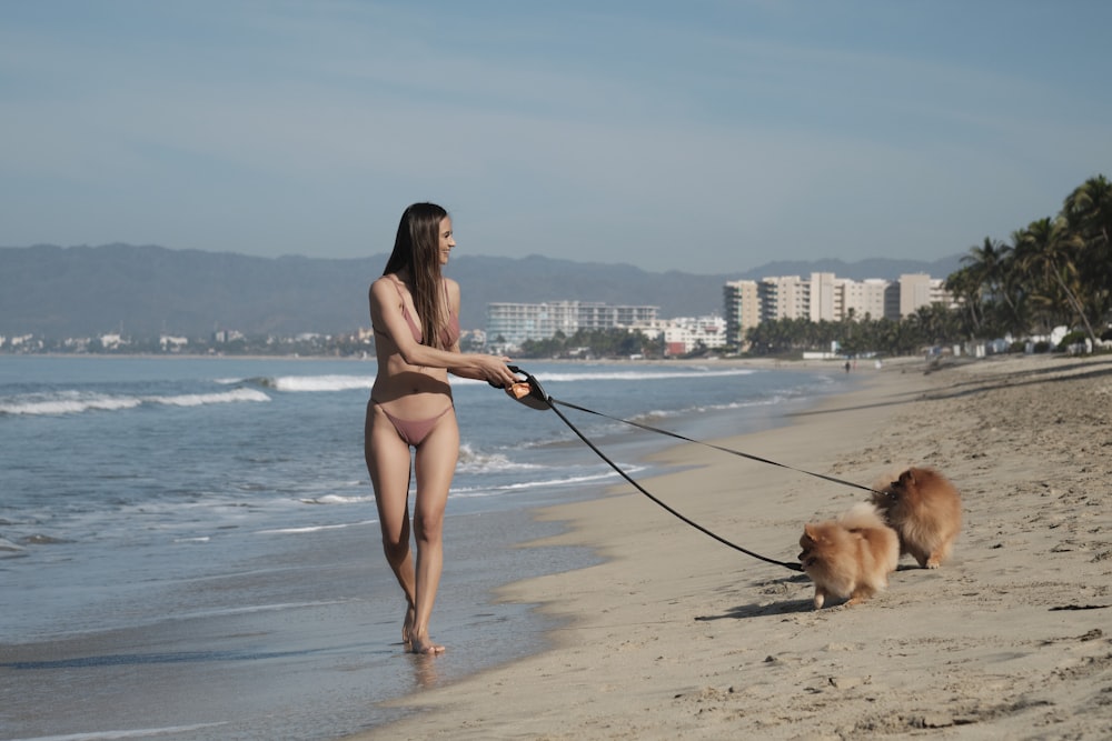 a woman walking a dog on a leash on the beach