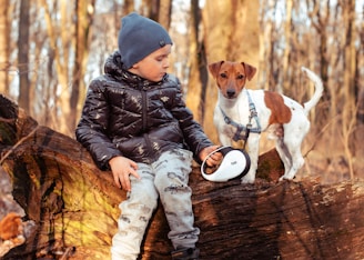 a little boy sitting on a log with a dog