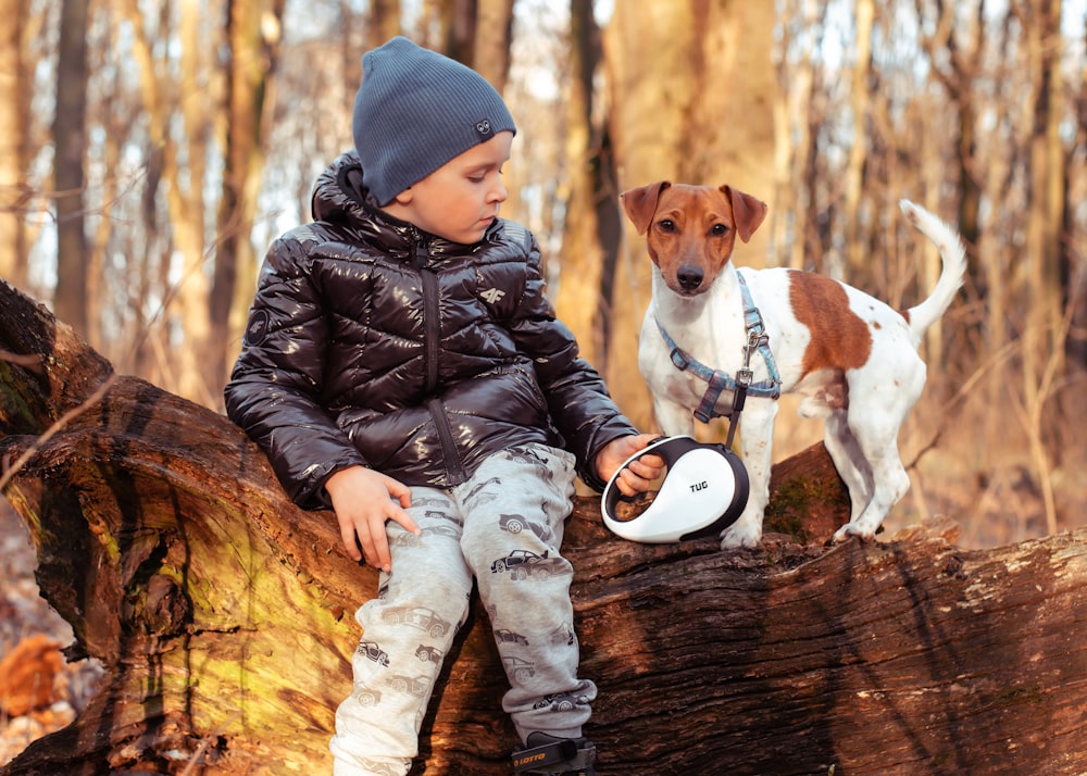 a little boy sitting on a log with a dog
