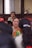 Several women are seated indoors, with one woman in the foreground wearing traditional clothing, appearing to hold a pair of glasses. The focus is on her as others are slightly blurred, possibly indicating a gathering or meeting.