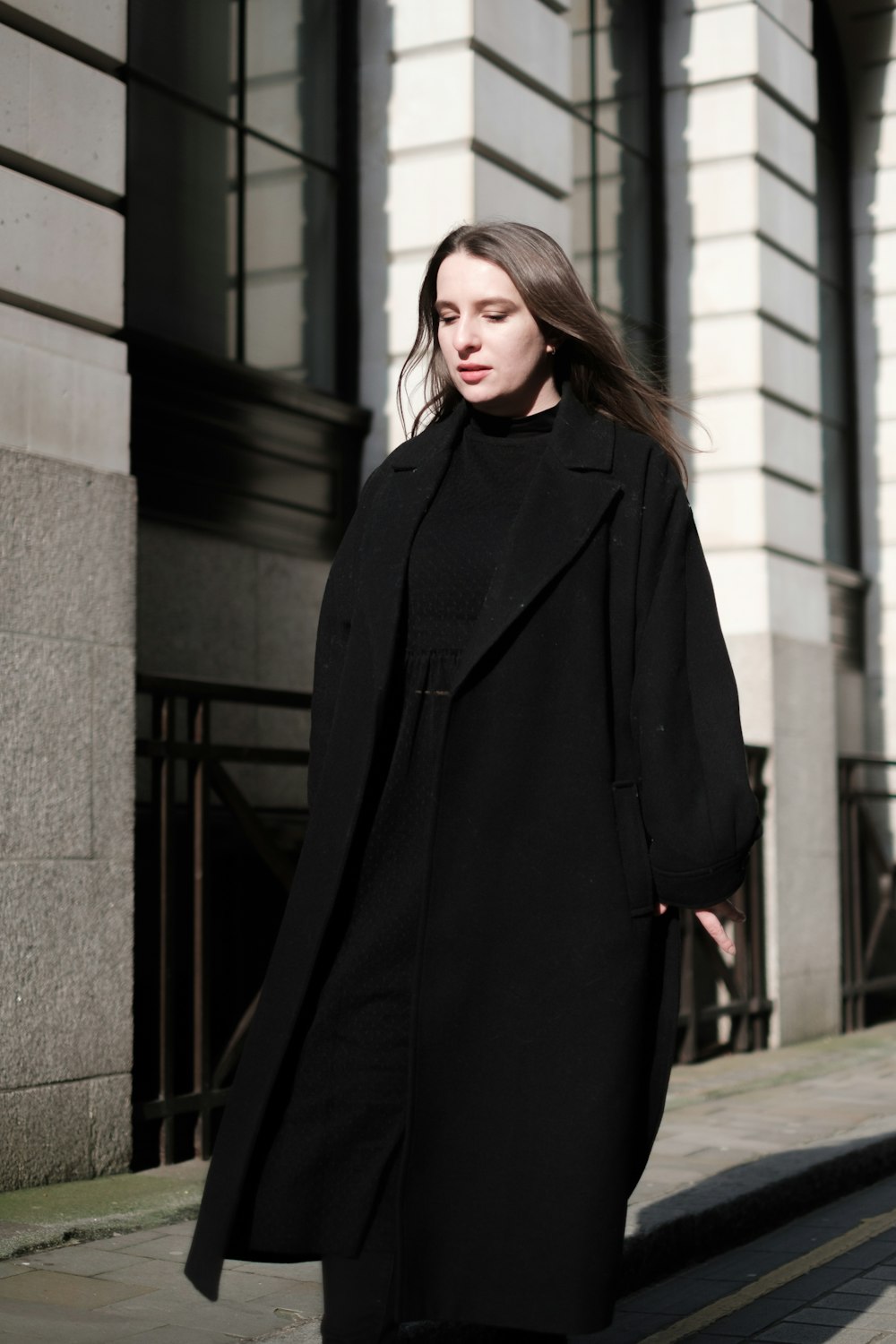 a woman in a black coat is walking down the street