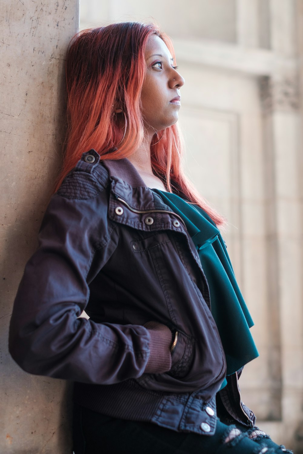 a woman with red hair leaning against a wall