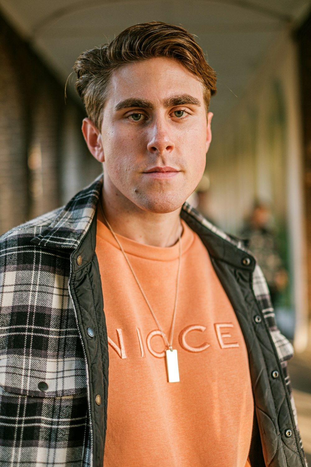 a young man wearing an orange shirt and a plaid jacket